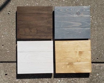 May include: Four square wooden signs with different paint colors. The signs are brown, gray, white, and light brown.