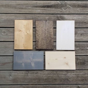 May include: Five rectangular wooden planks in different colours and finishes are arranged on a weathered wood surface. The planks include natural, stained, and painted options in shades of light brown, dark brown, white, grey, and light beige.