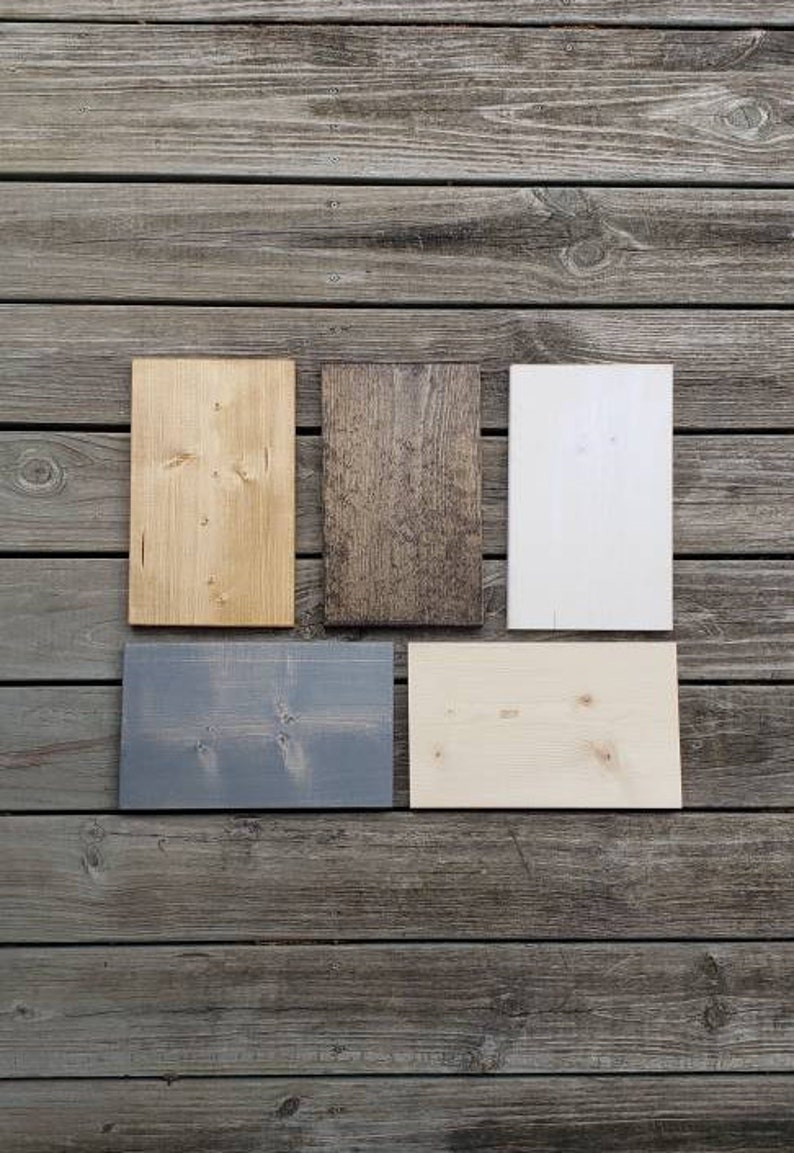 May include: Five rectangular wooden planks in different colours and finishes are arranged on a weathered wood surface. The planks include natural, stained, and painted options in shades of light brown, dark brown, white, grey, and light beige.