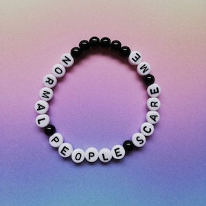Peut inclure: Un bracelet en perles blanches et noires avec les mots "Normal People Scare Me" écrits dessus.