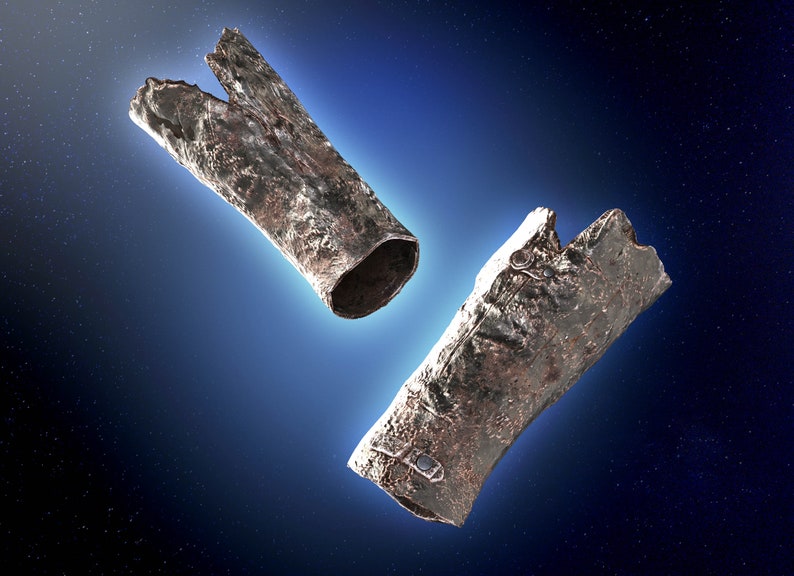 May include: Two pieces of metallic debris, possibly from a spacecraft, floating in space against a dark blue background with stars. The debris is silver and has a rough, textured surface.