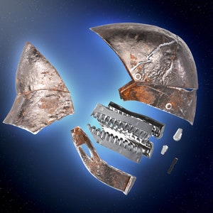 May include: A rusty metal helmet broken into multiple pieces against a dark blue starry background. The helmet is made of metal and has a rough, textured surface. The pieces are scattered around the centre of the image.