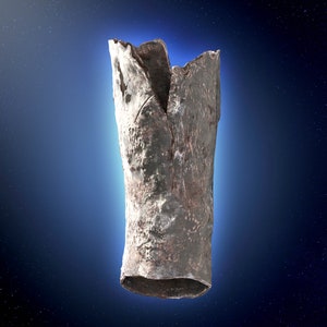 May include: A silver-coloured, cylindrical, metal object with a rough, textured surface. The object is cracked and broken at the top. It is photographed against a dark blue background with white stars.