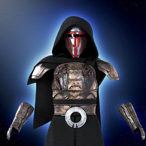 Op de afbeelding: Een zwarte, gekapte figuur die een rood en zilveren helm draagt met een donker, verweerd pantser en een zilveren riem met een cirkelvormig ontwerp. De figuur staat tegen een donkerblauwe achtergrond met witte sterren.