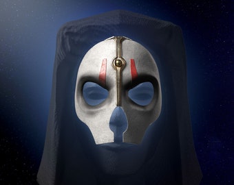Könnte beinhalten: Eine weiße Maske mit goldenem und rotem Design, getragen von einer Figur in einer dunklen Kapuzenrobe. Die Maske hat eine schädelartige Form mit Augenlöchern und einem prominenten Nasensteg.