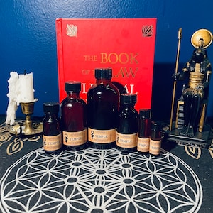 Puede incluir: Seis pequeñas botellas de vidrio con líquido oscuro en su interior, etiquetadas como "The Empress of the Hierophant Temple". Las botellas están dispuestas en círculo sobre una superficie con un patrón blanco y negro. Un libro rojo con letras doradas que dice "The Book of Law" está en el fondo. Una estatua negra de un dios egipcio con un tocado dorado está en el lado derecho de la imagen.