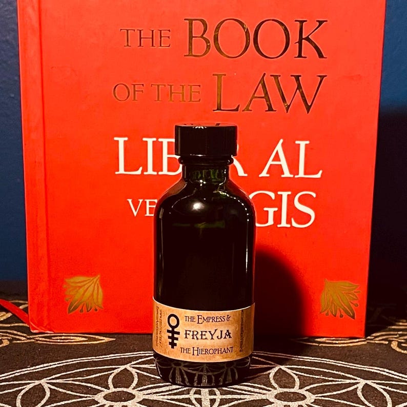 May include: A small, dark glass bottle with a black cap. The bottle has a label that reads "THE EMPRESS & FREYJA THE HIEROPHANT".