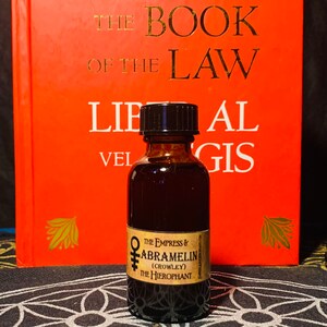 Puede incluir: Una peque&ntilde;a botella de vidrio marr&oacute;n con una tapa negra, que contiene un l&iacute;quido oscuro. La botella tiene una etiqueta con el texto "THE EMPRESS & ABRAMELIN (CROWLEY) THE HIEROPHANT".