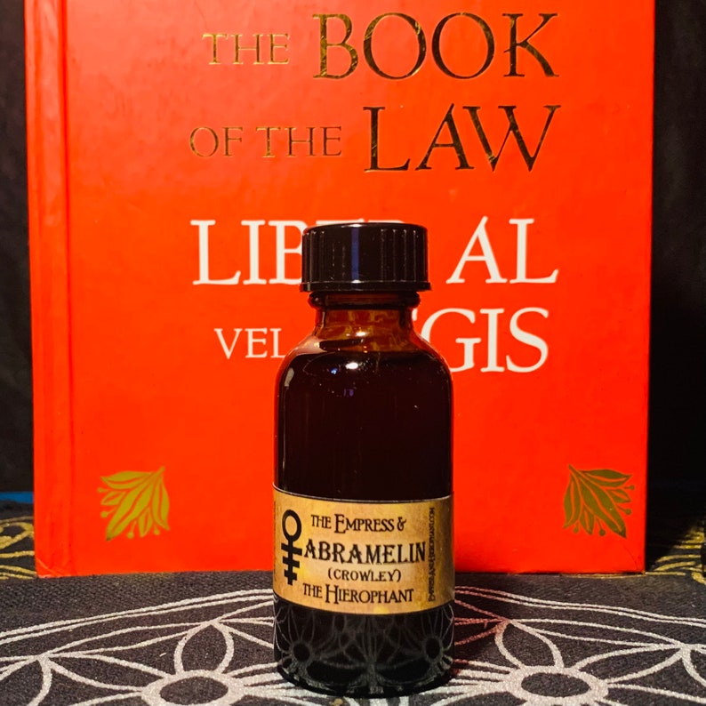 Puede incluir: Una peque&ntilde;a botella de vidrio marr&oacute;n con una tapa negra, que contiene un l&iacute;quido oscuro. La botella tiene una etiqueta con el texto "THE EMPRESS & ABRAMELIN (CROWLEY) THE HIEROPHANT".