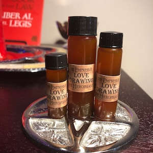 Könnte beinhalten: Drei kleine Glasflaschen mit brauner Flüssigkeit, jede mit einem Etikett mit der Aufschrift "The Empress & Love Drawing The Hierophant". Die Flaschen stehen auf einem silbernen Tablett mit einem Sternmuster.