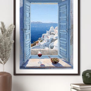 Könnte beinhalten: Gerahmter Kunstdruck einer malerischen Aussicht durch ein Fenster. Das Gemälde zeigt ein Küstendorf mit weißen Gebäuden und blauen Fensterläden. Ein Glas Rotwein und eine Schale Oliven stehen auf der Fensterbank, mit dem Meer im Hintergrund.