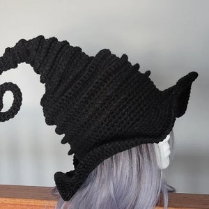 Puede incluir: Sombrero de bruja de ganchillo negro con un ala larga y rizada. El sombrero est&aacute; hecho con un punto texturizado y tiene una corona puntiaguda.