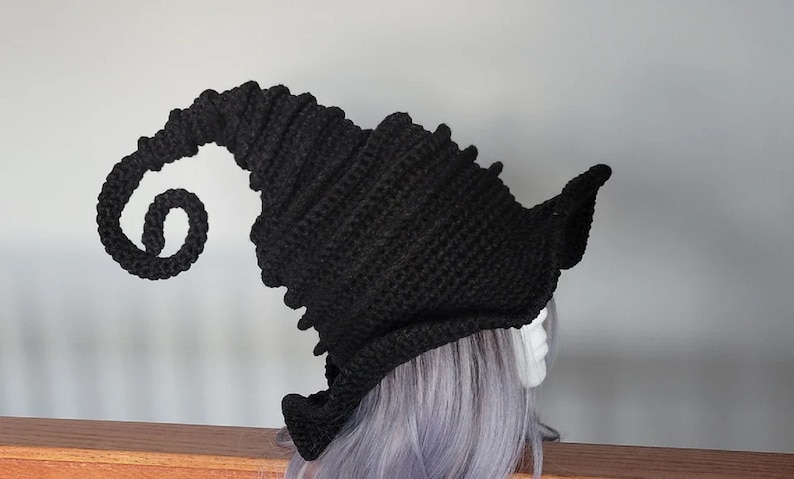 Puede incluir: Sombrero de bruja de ganchillo negro con un ala larga y rizada. El sombrero est&aacute; hecho con un punto texturizado y tiene una corona puntiaguda.