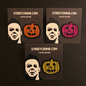 May include: Three black cards with the text "STREETCRUMB.COM LIMITED EDITION" printed on them. Each card features a black and white silhouette of Michael Myers from the Halloween franchise and a glitter pumpkin. The pumpkins are orange, pink, and gold.