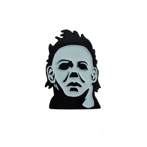 May include: Black and white enamel pin featuring a close-up of Michael Myers' mask from the Halloween horror film franchise.