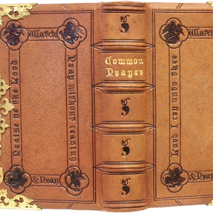 Puede incluir: Libro antiguo encuadernado en cuero abierto, con protectores de esquina y un cierre de metal dorado. El libro es de color marr&oacute;n claro con texto en relieve y elementos decorativos. El lomo dice "Common Prayer."