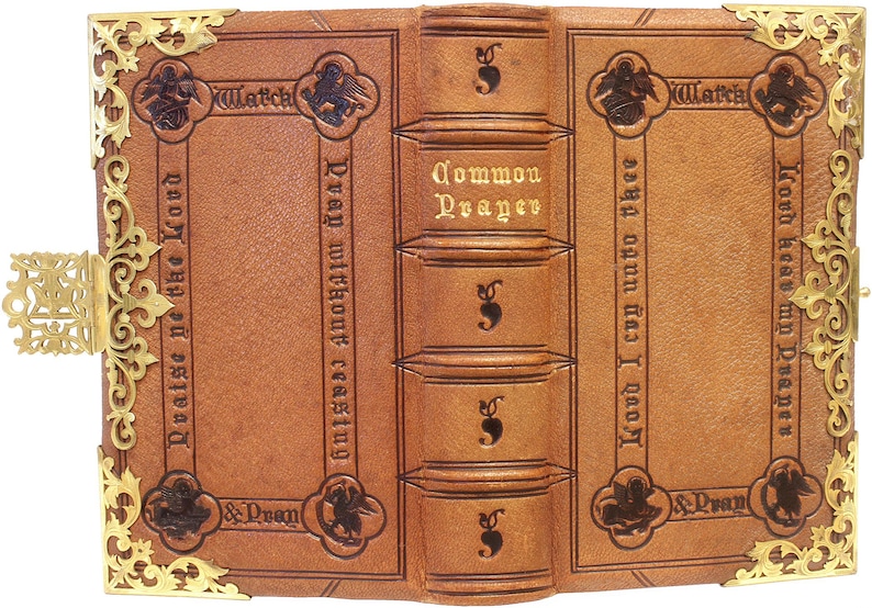 Puede incluir: Libro antiguo encuadernado en cuero abierto, con protectores de esquina y un cierre de metal dorado. El libro es de color marr&oacute;n claro con texto en relieve y elementos decorativos. El lomo dice "Common Prayer."
