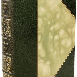 Puede incluir: Libro antiguo con cubierta de cuero verde oscuro y detalles dorados. La columna vertebral presenta texto en relieve y elementos decorativos. La portada tiene un dise&ntilde;o verde claro y dorado. El libro se titula "Emerson's Works VI" y "Conduct of Life".