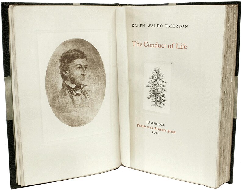 Puede incluir: Libro abierto con cubierta negra. La p&aacute;gina izquierda presenta un retrato en sepia de Ralph Waldo Emerson en un marco ovalado. La p&aacute;gina derecha muestra el t&iacute;tulo "The Conduct of Life" y una peque&ntilde;a ilustraci&oacute;n de un &aacute;rbol. Impreso en Cambridge en 1904.