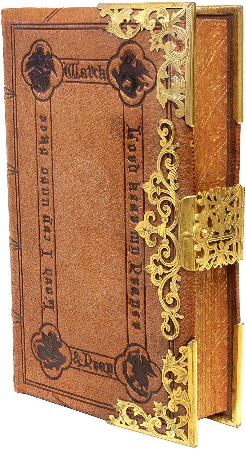 Puede incluir: Libro antiguo encuadernado en cuero con detalles met&aacute;licos dorados. La portada presenta texto en relieve y esquinas decorativas. El libro tiene un cierre y filigranas ornamentadas. El texto de la portada dice "Lord hear my Prayer" y "Watch".
