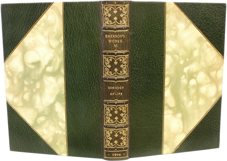 Puede incluir: Un libro antiguo titulado "Emerson's Works VI Conduct of Life" con una cubierta de cuero verde oscuro. El lomo es marr&oacute;n con letras doradas y elementos decorativos. El a&ntilde;o "1904" est&aacute; impreso en la parte inferior.