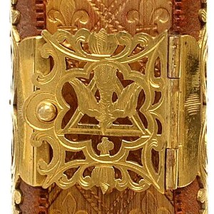 Puede incluir: Primer plano detallado de una cubierta de libro decorativa. La cubierta es de un marr&oacute;n dorado c&aacute;lido con un patr&oacute;n de flor de lis repetido. Los detalles met&aacute;licos dorados y un cierre se suman a la est&eacute;tica antigua. El libro mide aproximadamente 25 cm de alto.