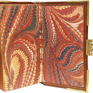 Puede incluir: Libro antiguo abierto con p&aacute;ginas de papel jaspeado en tonos rojo, negro y crema. El libro tiene una cubierta de cuero marr&oacute;n con protectores de esquina de metal dorado y un cierre decorativo. Las p&aacute;ginas muestran un patr&oacute;n arremolinado.