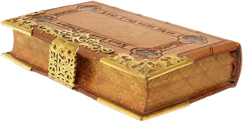 Puede incluir: Un libro antiguo con una cubierta de cuero marr&oacute;n claro y detalles met&aacute;licos dorados. El libro tiene esquinas decorativas y un cierre. Los bordes de las p&aacute;ginas est&aacute;n dorados. La cubierta tiene texto en relieve y elementos decorativos.