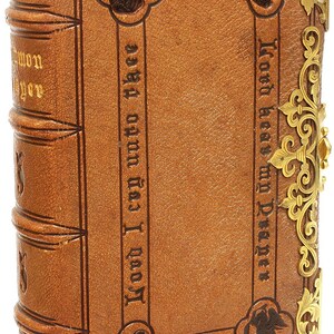 Puede incluir: Antiguo libro encuadernado en cuero marr&oacute;n con esquinas de metal dorado. La cubierta presenta texto en relieve y motivos decorativos de &aacute;ngeles. El lomo tiene bandas en relieve y letras doradas. El libro est&aacute; cerrado.