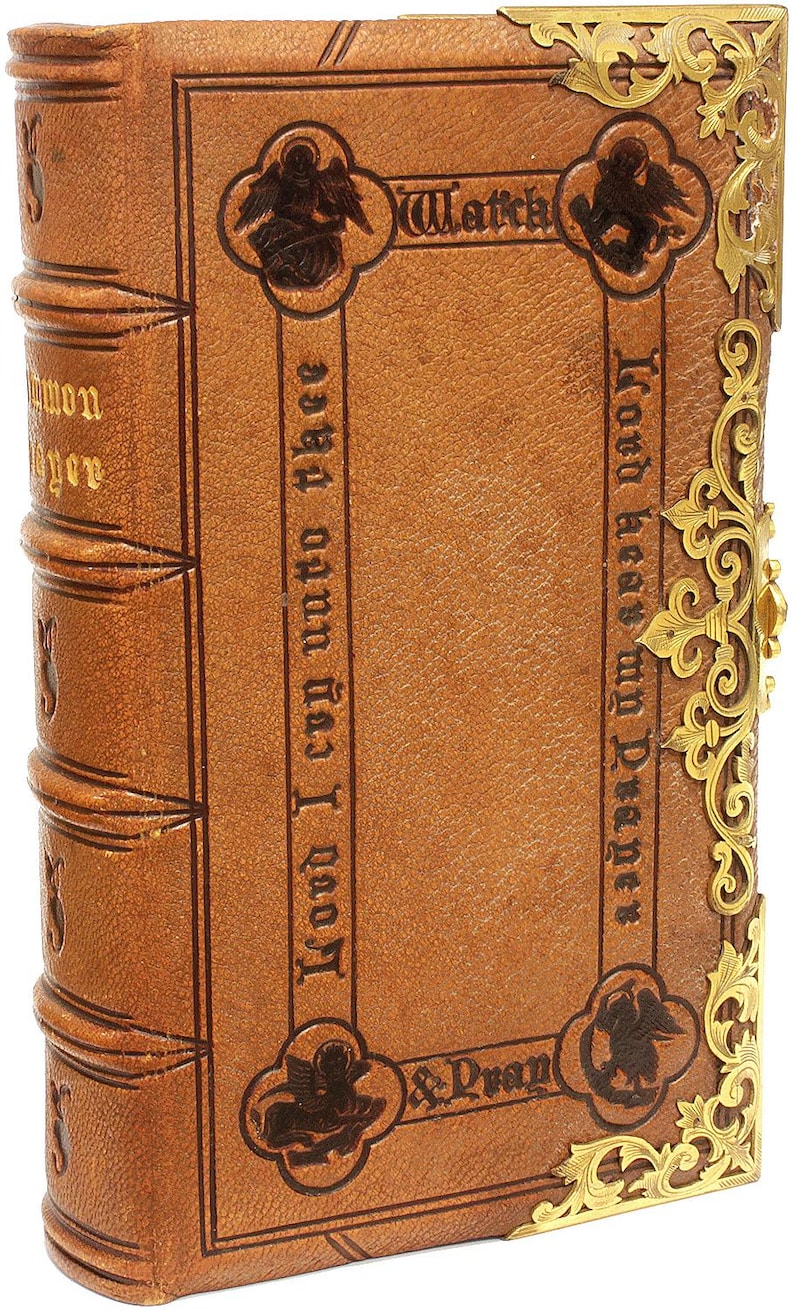 Puede incluir: Antiguo libro encuadernado en cuero marr&oacute;n con esquinas de metal dorado. La cubierta presenta texto en relieve y motivos decorativos de &aacute;ngeles. El lomo tiene bandas en relieve y letras doradas. El libro est&aacute; cerrado.
