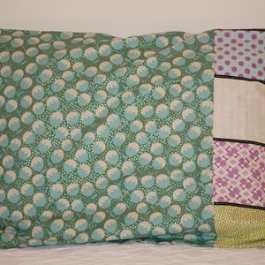 May include: A green pillow with a white and gold floral pattern. The pillow has a patchwork design on the right side with pink, white, and green fabric.