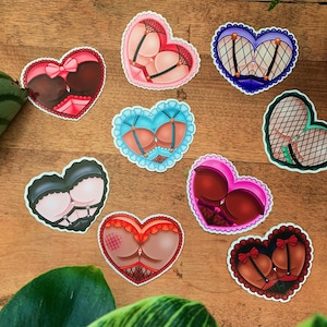 May include: Nine heart-shaped stickers with illustrations of lingerie. Each sticker features a different colour and design, including black, red, blue, and green.