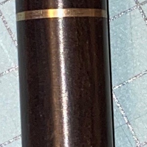 May include: A dark brown, cylindrical object with a gold band. The object has a smooth, polished surface and a rounded top. It appears to be a container or a part of a larger item.
