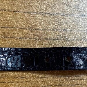 May include: Black leather watch band with a crocodile pattern and the number "87323" embossed on it.