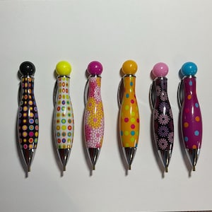 May include: Set of six colorful pens with a polka dot design. Each pen has a different color top and a silver tip.