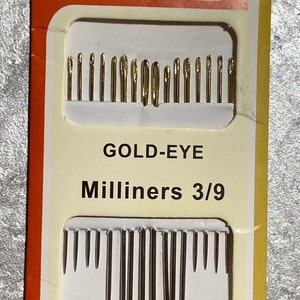 May include: A package of gold-eye milliners needles. The package is white with orange and yellow accents. The text on the package reads "TQLYRA", "NEEDLES", "GOLD-EYE Milliners 3/9", and "16 Needles". The needles are arranged in two rows.