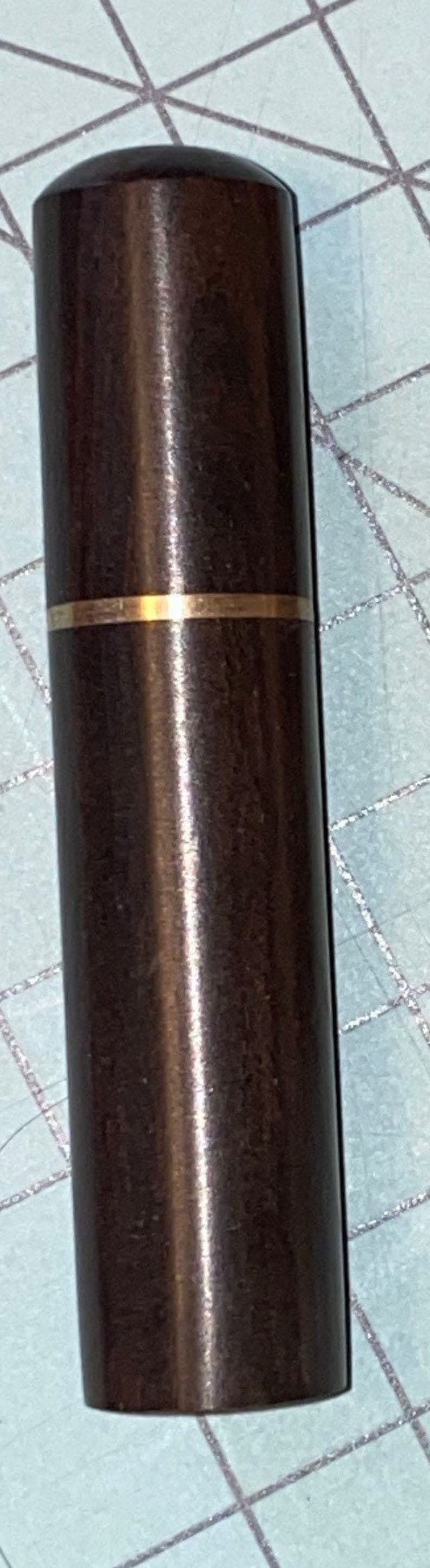 May include: A dark brown, cylindrical object with a gold band. The object has a smooth, polished surface and a rounded top. It appears to be a container or a part of a larger item.