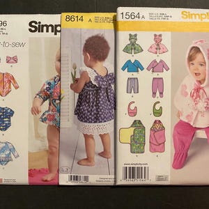 May include: Three Simplicity sewing patterns featuring children's clothing. The first pattern is for a swimsuit, the second is for a dress, and the third is for a hooded cape. The patterns are all on yellow paper with black text and illustrations.