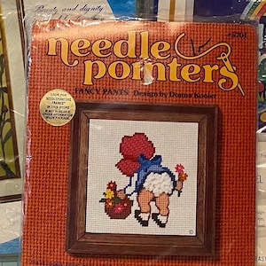Könnte beinhalten: Ein Kreuzstich-Set namens "Needlepointers Fancy Pants" mit einem gerahmten Design eines Kindes, das Blumen pflückt. Das Set enthält ein gedrucktes Design, Leinwand, Wolle und Anweisungen.
