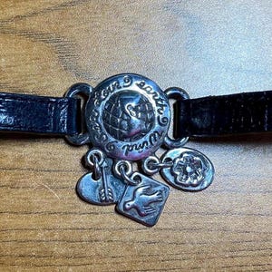 May include: A black leather bracelet with a silver charm that says "Loved by earth" and has a dove design. The bracelet has a silver buckle.