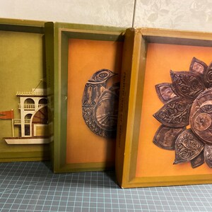 Könnte beinhalten: Drei gerahmte Kunstwerke mit Vintage-Ästhetik. Das erste zeigt ein Boot mit roter Flagge, das zweite einen Vogel und das dritte eine Sonne mit Gesicht. Jedes Stück ist vor einem warmfarbigen Hintergrund platziert und grün-gold gerahmt.