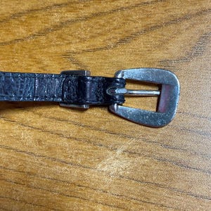 May include: A black leather belt with a silver buckle. The buckle is a simple, rectangular design.