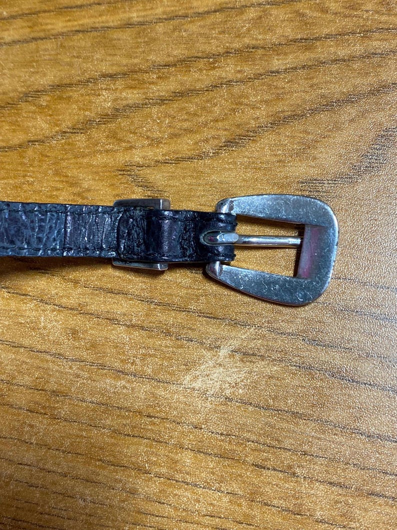 May include: A black leather belt with a silver buckle. The buckle is a simple, rectangular design.
