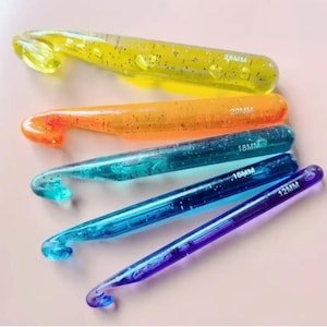 May include: Set of five colorful crochet hooks with glitter embedded in the plastic. The hooks are sized 12mm, 16mm, 18mm, 20mm, and 24mm.