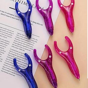 May include: Five colourful pens with a unique design. The pens have a clear plastic body with glitter embedded in the plastic. The pens have a unique design with a loop at the top that can be used to hold the pen.