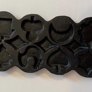 May include: A black cast iron mold with various shapes, including hearts, diamonds, clubs, spades, and a Christmas tree. The mold is designed for making decorative cookies or candies.