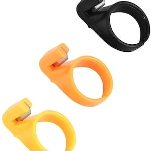 May include: Three finger thread cutters, two are orange and one is black. The thread cutters are designed to be worn on the finger and have a small blade to cut thread.