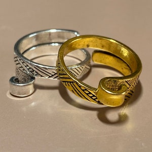 May include: Two adjustable rings with a geometric pattern. The ring on the left is silver and the ring on the right is gold.