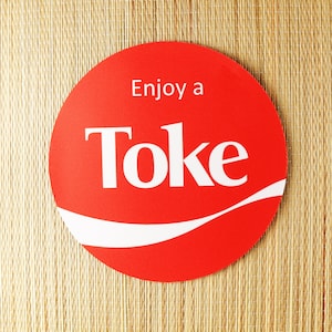 May include: Red and white circle with the text "Enjoy a Toke" in white letters. The circle has a white swoosh design.