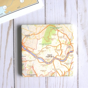 May include: A map of Seoul, South Korea, with the city's districts labeled in Korean and English. The map is printed on a white ceramic coaster.